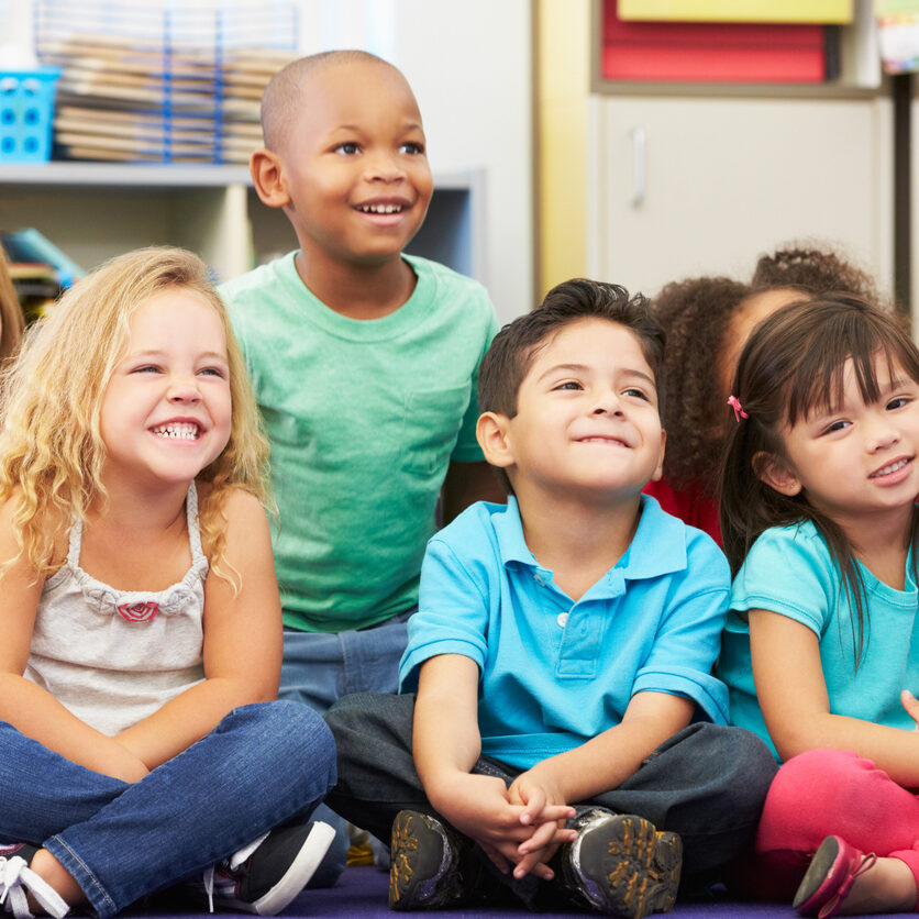 Group of Elementary Pupils In Classroom Sitting Down Looking Away From Camera Smiling